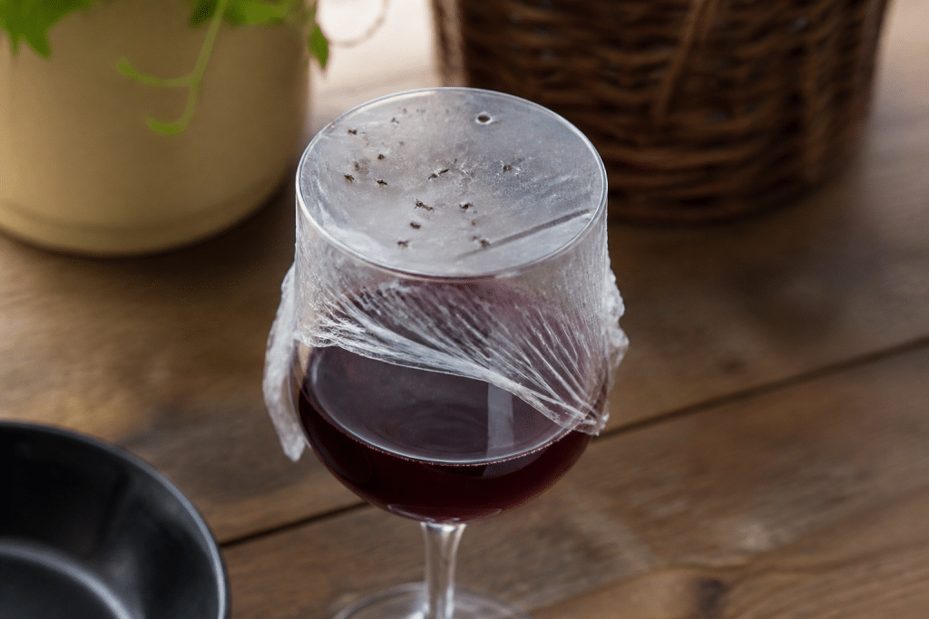 Verre de vin rouge recouvert film percé piège moucherons